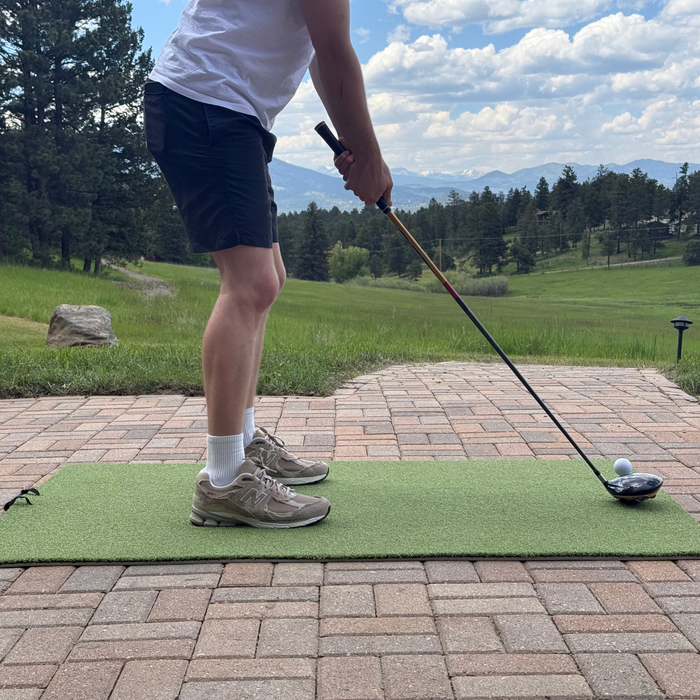A man practicing golf in his backyard. Standing on a turf hitting mat with a driver