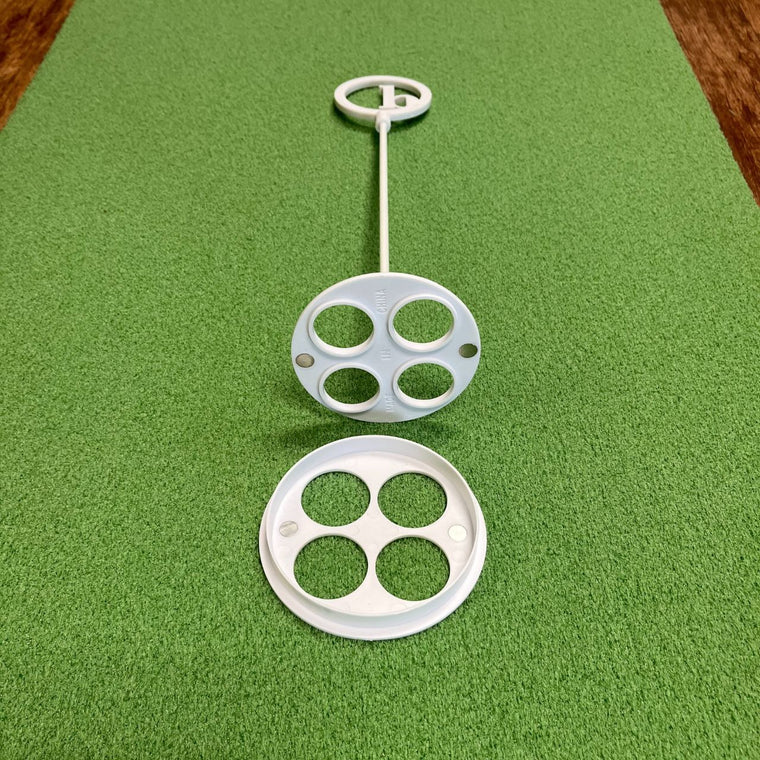 A BirdieBall Putting Green Cups and Flags set in white plastic, featuring circular holes, rests on a textured green surface with one cup separated and facing upward.
